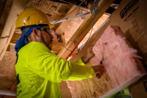 Fiberglass insulation installer installing insulation into wall